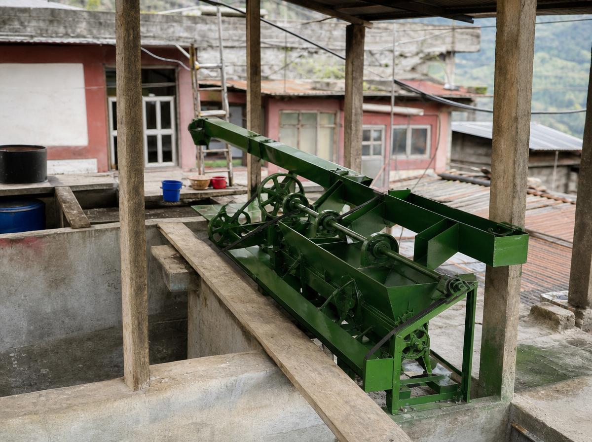 A green cast-iron coffee depulping machine with belts and flywheels on a concrete wet-mill terrace in a Nepali hill town.
